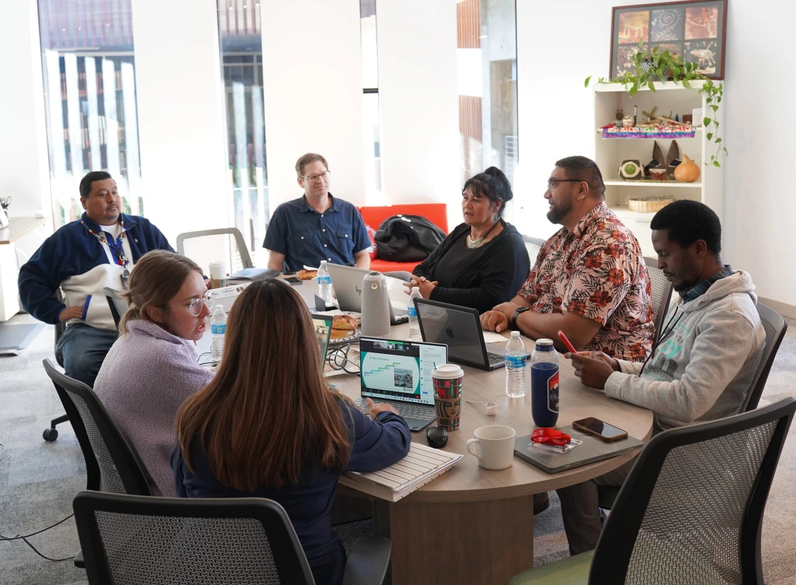 7 people sitting around a conference room table having a discussion.